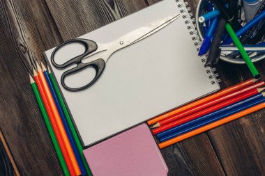 Tahta bir masanın üzerindeki kırtasiye kağıdı açık not defteri makasları renkli kalemler notu