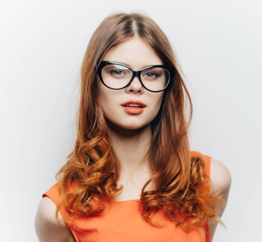 Kırmızı saçlı, turuncu elbiseli, makyajlı, gözlüklü bir kadın.