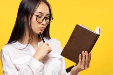 Asyalı bir kadın elinde kalemle resmî sarı bir arkaplan tutuyor.