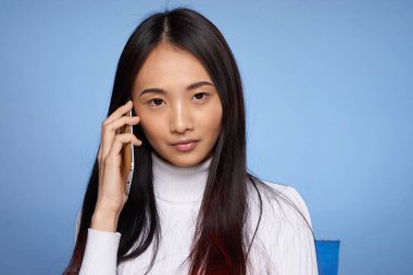 Asyalı kadın telefon teknolojisi stüdyo mavi arka planda konuşuyor.