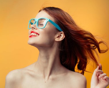 Turuncu arka planda parlak makyajlı mavi gözlüklü mutlu kadın.