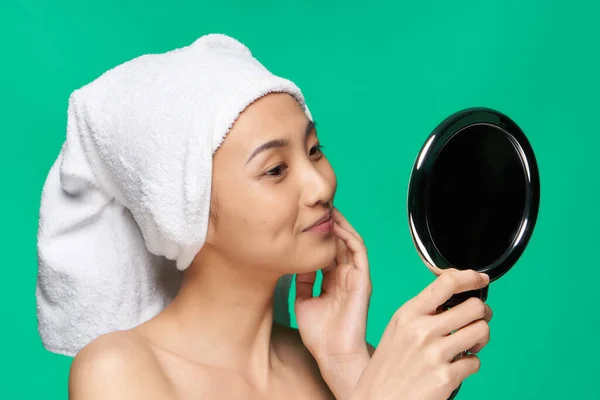 동양의 외모를 하고 있는 여자가 수건으로 머리를 닦고 거울 속을 들여다 본다 — 스톡 사진
