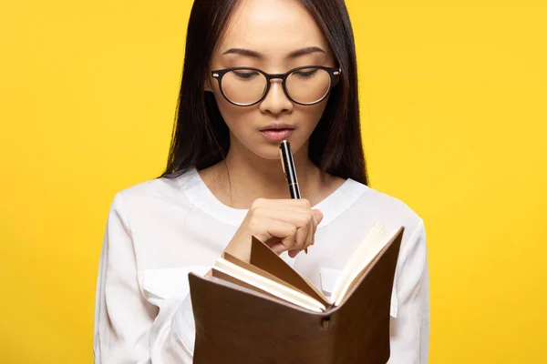 Zakelijke vrouw met een notebook in haar handen houdt een pen in de buurt van haar lippen elegante stijl gele achtergrond — Stockfoto