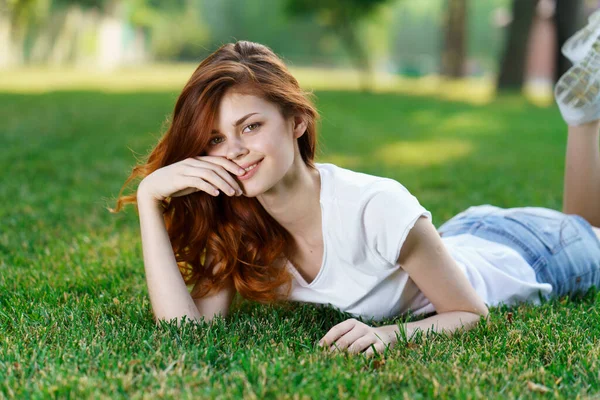Frau liegt auf dem Rasen im Park und hat Handy in der Hand — Stockfoto