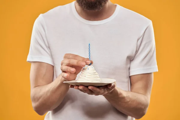 Um homem com um bolo de aniversário em suas mãos em uma sobremesa de aniversário de fundo amarelo — Fotografia de Stock