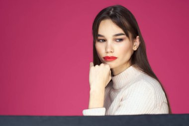 Uzun saçlı, kırmızı dudaklı beyaz bluzlu, pembe arka planlı çekici bir kadın.