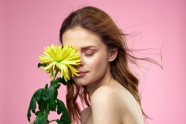 Pembe arka planda sarı çiçekli güzel bir kız çıplak omuzlarına makyaj yapıyor.