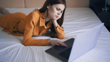 Kadın yatak odasında yatar dizüstü bilgisayarın önünde çalışır.