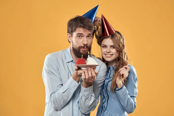 Anniversaire partie homme et femme sur un fond jaune dans des chapeaux avec un gâteau dans leurs mains — Photo