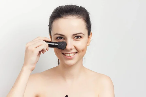 Woman with bare shoulders applying makeup brush on face — Stock Photo, Image