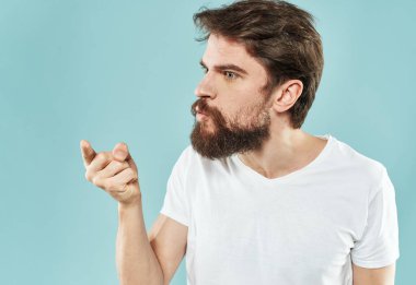 Mavi arka planda beyaz tişörtlü esmer adam şaşırmış görünüyor.