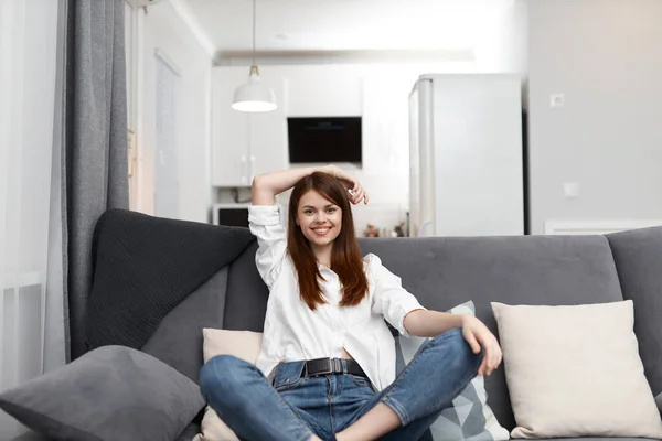 Sorrindo mulher sentada no sofá com almofadas confortável apartamento tempo livre — Fotografia de Stock