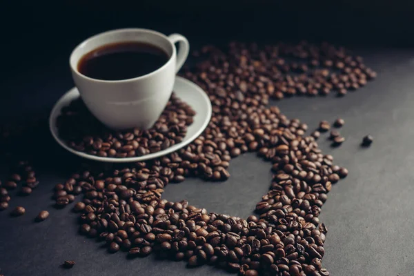 Corazón extraído de granos de café y una taza con un desayuno platillo bebida en la cama — Foto de Stock