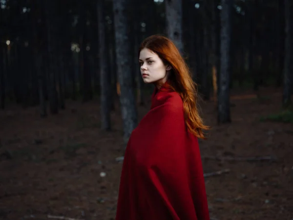 一位红头发、肩上扛着格子花的女人走在树旁的森林里 — 图库照片