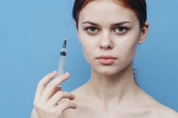 Kvinna med en spruta i handen gör injektioner i ansiktet på en blå bakgrund botox operation — Stockfoto