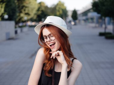 Beyaz şapkalı ve gözlüklü mutlu kadın sokaklarda yürüyor.