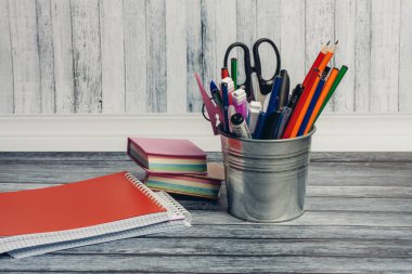 Demirden bir kavanozda kırtasiye malzemeleri ve ofisteki ahşap bir masada not defterleri.