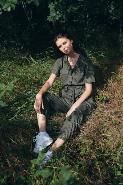 Ωραία γυναίκα κάθεται στο γρασίδι στο δάσος με φόρμες και αθλητικά παπούτσια — Φωτογραφία Αρχείου