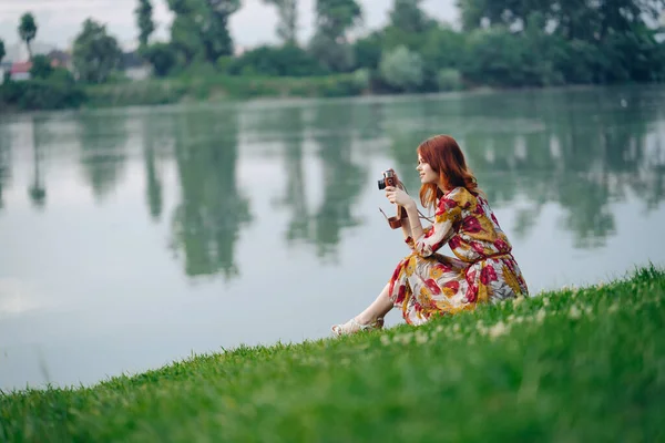 Donna all'aperto in un abito con una macchina fotografica in mano sulla riva del lago di vacanza — Foto Stock