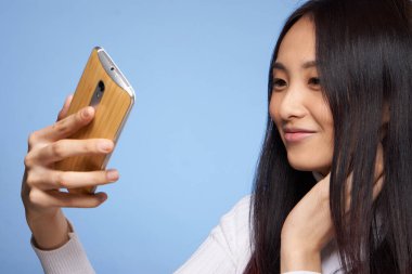 Kadın Asyalı görünüm telefonu elinde internetle iletişim kuruyor mavi arka plan