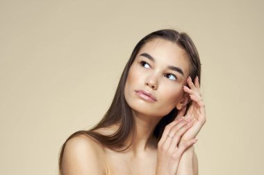 Esmer, çıplak omuzlu, yakın plan uzun saçlı, bej arkaplan temiz ciltli.