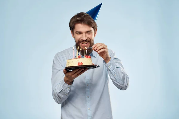 Hombre barbudo con un plato de pastel sobre un fondo azul y un sombrero de fiesta de cumpleaños en su cabeza — Foto de Stock