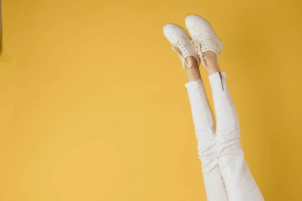 Patas femeninas jeans blancos zapatillas moda fondo amarillo ver —  Fotos de Stock