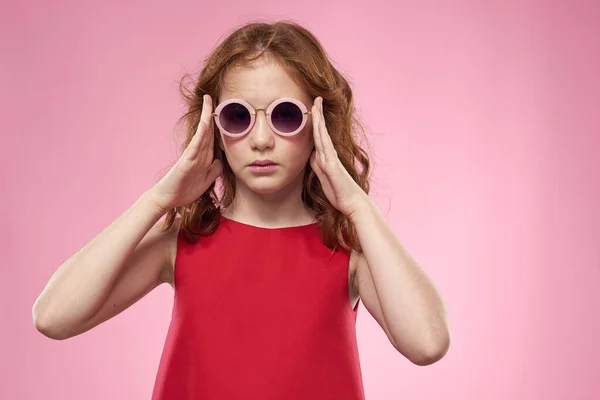 Mädchen mit lockigem Haar dunkle runde Brille Spaß rotes Kleid rosa Hintergrund — Stockfoto