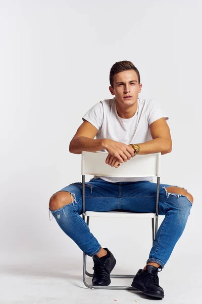 Een man in jeans zit op een stoel achterover en scheurt jeans T-shirt vooraanzicht — Stockfoto