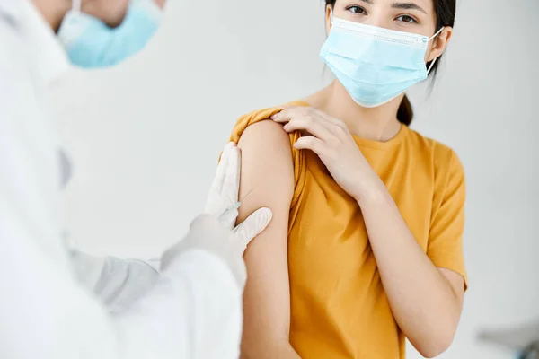 Médico injetando uma mulher em uma camiseta amarela no ombro close-up vacinação vívida — Fotografia de Stock