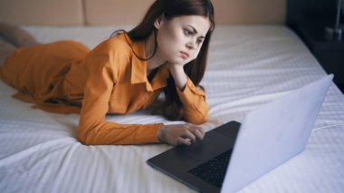 Kadın yatak odasında yatar dizüstü bilgisayarın önünde çalışır.