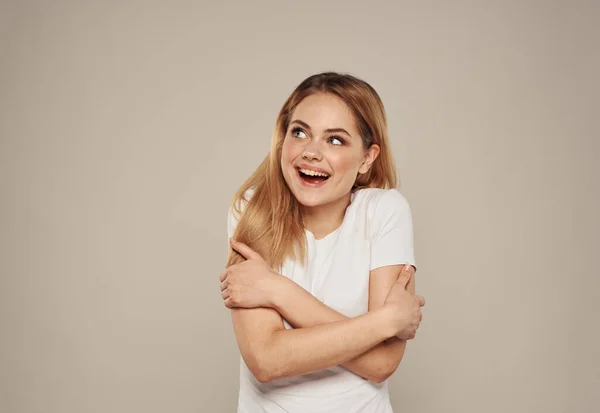 Mulher de t-shirt branca no fundo bege abraça-se com as mãos vista cortada — Fotografia de Stock