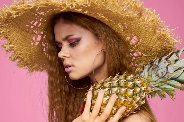 Kvinna med en pistol i händerna på en halm hatt ljus makeup exotiska frukter sommar rosa bakgrund — Stockfoto