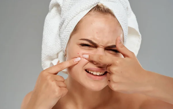 Emotionale Frau mit Handtuch auf dem Kopf quetscht Pickel im Gesicht vor grauem Hintergrund aus — Stockfoto