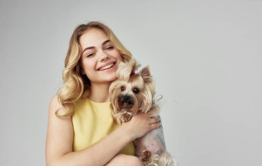 Sarı elbiseli bir kadın kucağında küçük bir köpek tutuyor.