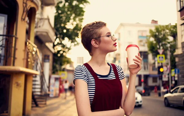 Bonita mujer con el pelo corto y labios rojos en la calle caminar vidrio con bebida — Foto de Stock