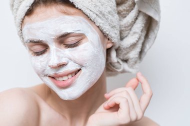 Çıplak omuzlu, başı havluyla cilt bakımı maskeli bir kadın.