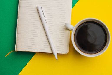 Renkli arka planda kahve fincanı ve not defteri üst görünüm ofisi.