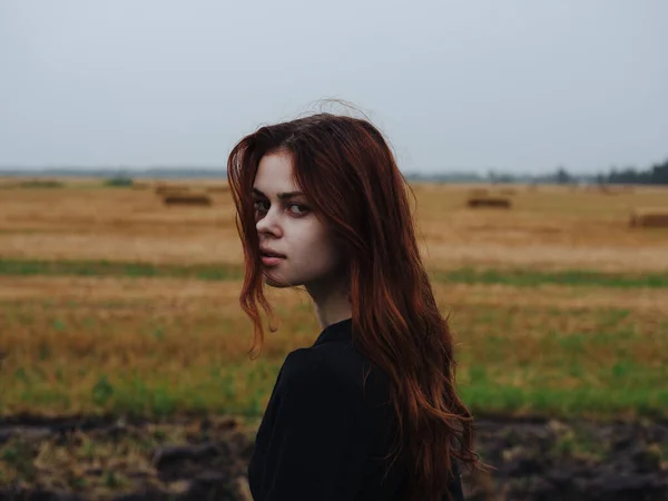 Portrait d'une femme aux cheveux roux vêtue d'une robe noire dans un champ en pleine nature vue dégagée — Photo