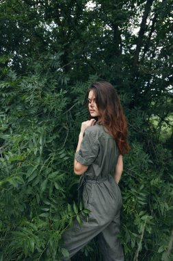 Çalılıkların yakınındaki yeşil tulumlu bir kadının portresi temiz hava ile kendine dokunuyor. 