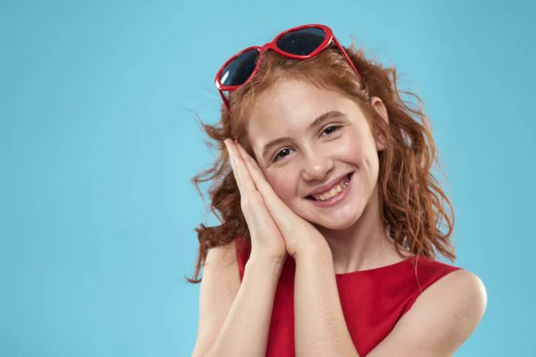 Mädchen mit lockigem Haar Sonnenbrille rotes Kleid und Kindheit Spaß blauen Hintergrund — Stockfoto