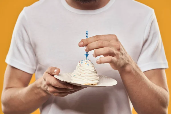 Um homem com um bolo de aniversário em suas mãos em uma sobremesa de aniversário de fundo amarelo — Fotografia de Stock