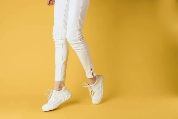 Mulheres pernas calças brancas sapatilhas moda roupas luxo rua estilo amarelo fundo — Fotografia de Stock