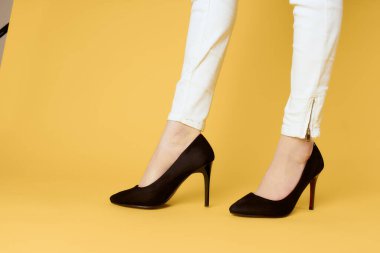 Siyah ayakkabılı kadın bacakları kırpılmış sarı arka plan moda alışverişi