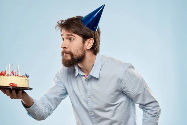 Un hombre con una camisa con un pastel en las manos y una gorra festiva en la cabeza — Foto de Stock