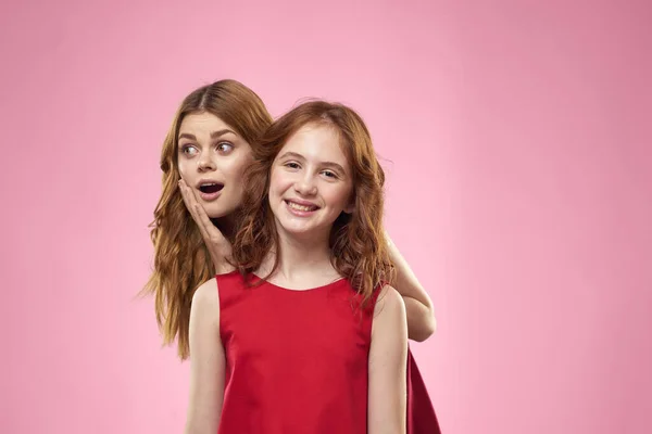 Fröhliche Mutter und Tochter in roten Kleidern stehen neben fröhlicher Familie auf rosa Hintergrund — Stockfoto