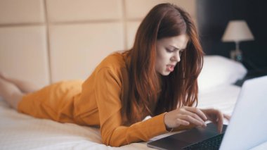 Yataktaki kadın dizüstü bilgisayarla yüz ifadesinden memnun değil.