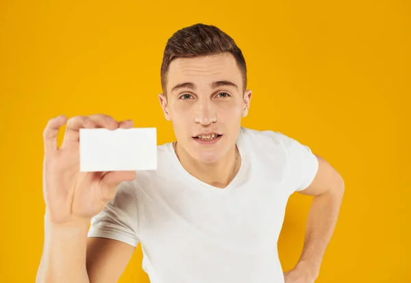 Facet w białym t-shirt pokazując wizytówkę na żółtym tle przycięte widok — Zdjęcie stockowe