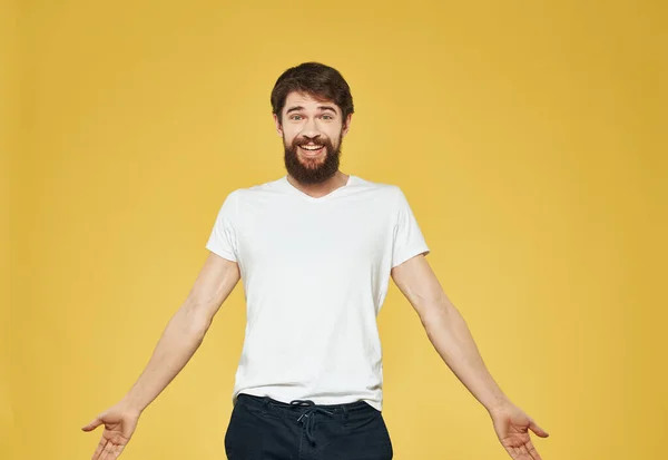 Ένας άντρας με γενειάδα κάνει χειρονομίες με τα χέρια του σε κίτρινο φόντο και τα σκούρα παντελόνια είναι μοντέλο. — Φωτογραφία Αρχείου