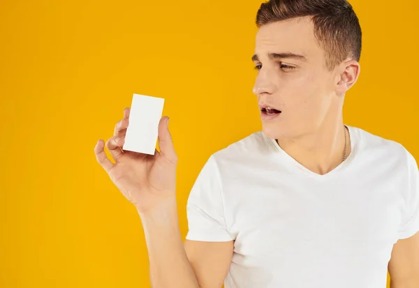 Mężczyzna w białym t-shirt pokazując wizytówkę na żółtym tle przycięte widok — Zdjęcie stockowe